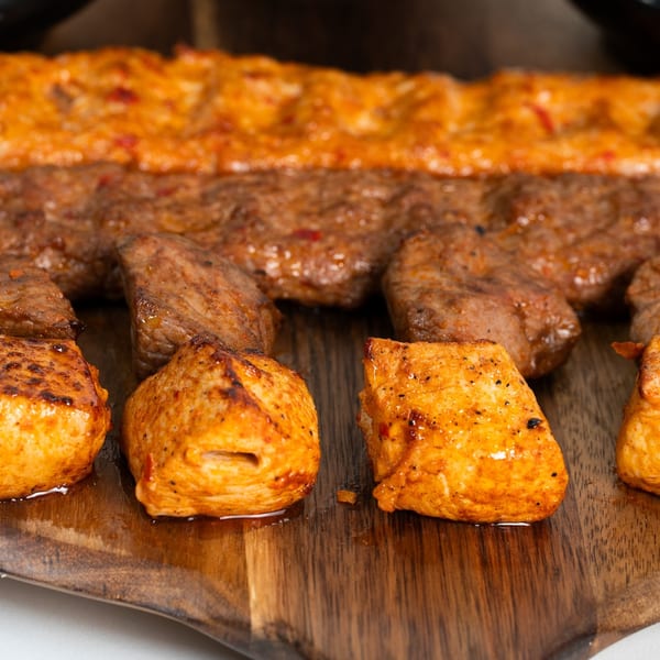 Close-up of Middle Eastern grilled chicken and beef kebabs on a wooden serving board.
