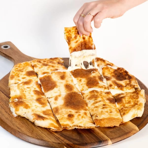 A hand pulls a cheesy slice of Middle Eastern flatbread from a wooden board, stretching the cheese.