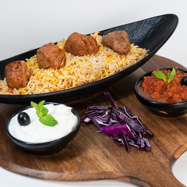 Middle-Eastern dish with meat chunks on rice, served with red cabbage, yogurt, and tomato sauce.