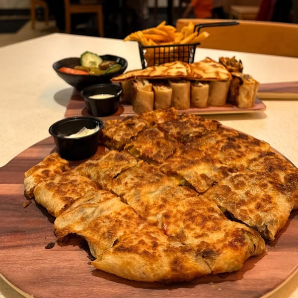 A large, golden-brown, square-cut middle-eastern flatbread with sides of fries, pickles, and sauces.