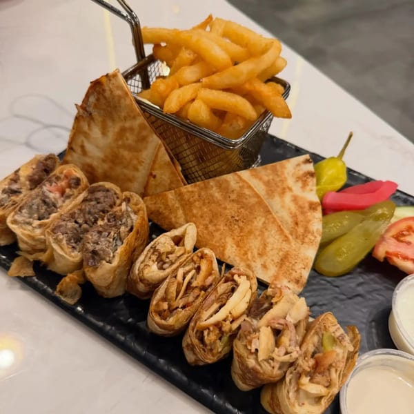 Middle-Eastern platter with shawarma wraps, pita bread, fries, pickles, and dipping sauces.