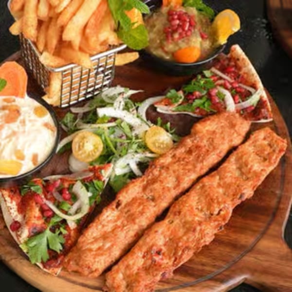 Middle-eastern platter with two long kebabs, fries, dips, and flatbread slices with pomegranate and onions.